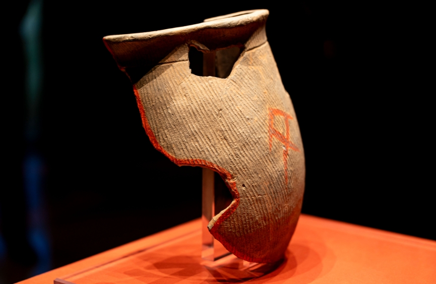 朱書扁壺（展廳中為復制品，真品現藏于中國考古博物館）。扁壺為泥質灰陶，器表飾細條豎藍紋，是陶寺先民打水的工具。這件破碎的扁壺有朱書文字位于兩面，十分珍貴。